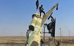 Fighters of the Islamic State waving the group's flag from a damaged display of a government fighter jet following the battle for the Tabqa air base, in Raqqa, Syria, in August 2014. (photo credit: AP/Raqqa Media Center of the Islamic State group)