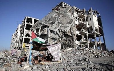 In this Monday, Aug. 11, 2014 file photo, Palestinian Ziad Rizk, sits with others in a shelter made of a blanket stretched over four poles next to one of the destroyed al-Nada Towers, where he lost his apartment and clothes shop, in the town of Beit Lahiya, northern Gaza Strip.  (photo credit: AP Photo/Khalil Hamra, File)