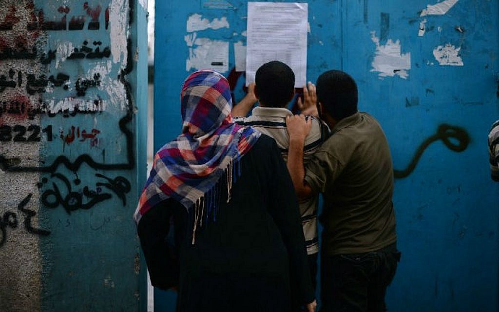Palestinians look at a list posted on a door to a UN school in Jabalia that gives information on food aid distribution schedules for people that have been displaced from their homes, August 11, 2014 (photo credit: AFP/Roberto Schmidt)