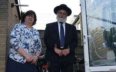 Rabbi Binyomin Jacobs and his wife, Bluma, by the glass window of their home damaged in an attack on July 17, 2014. (Cnaan Liphshiz/JTA)