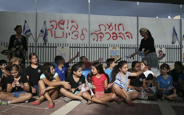 School children wave the Israeli flag as they sit in their school playground in front of a dividing barrier put up by the Beit Shemesh municipality, September 02, 2014. Graffiti reads "Separation barrier, a disgrace to Zionism" . (photo credit: Nati Shohat/Flash90) School children wave the Israeli flag as they sit in their school playground in front of a dividing barrier put up by the Beit Shemesh municipality, September 02, 2014. Graffiti reads "Separation barrier, a disgrace to Zionism" . (photo credit: Nati Shohat/Flash90)