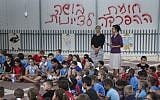 Schoolchildren wave the Israeli flag in their Beit Shemesh school playground, where graffiti on the fence reads, 'The segregation wall is a shame to Zionism,' September 2, 2014. (photo credit: Nati Shohat/Flash90)