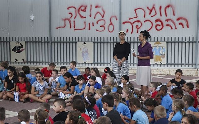 Schoolchildren wave the Israeli flag in their Beit Shemesh school playground, where graffiti on the fence reads, 'The segregation wall is a shame to Zionism,' September 2, 2014. (photo credit: Nati Shohat/Flash90) Schoolchildren wave the Israeli flag in their Beit Shemesh school playground, where graffiti on the fence reads, 'The segregation wall is a shame to Zionism,' September 2, 2014. (photo credit: Nati Shohat/Flash90)