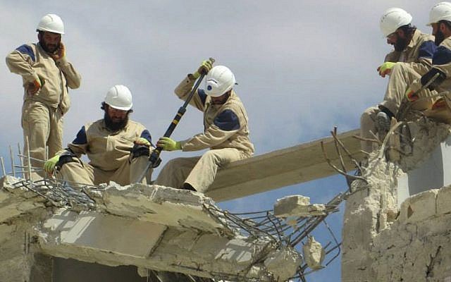 In this photo posted on September 21, 2014, provided by Civil Defense Idlib, a group of volunteers in northern Syria which has been authenticated based on its contents and other AP reporting, show Syrian civil defense workers with their white helmets, center, remove debris from a damaged building which was shelled by the Syrian government forces, in Idlib province, northern Syria.  (photo credit: AP/Civil Defense Idlib)