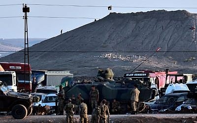 Islamic State (IS) militants (Rear) stand next to an IS flag atop a hill in the Syrian town of Ain al-Arab, known as Kobani by the Kurds, as seen from the Turkish-Syrian border, with Turkish troops in foreground, in the southeastern town of Suruc, Sanliurfa province, on October 6, 2014. (photo credit: AFP/ARIS MESSINIS)