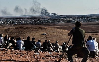 Kurdish people watch smoke billowing from Kobani as they gather upon a hill overlooking the Syrian town of Kobani, also known as Ain al-Arab, in the southeastern village of Mursitpinar, Sanliurfa province, on October 15, 2014.  (photo credit: AFP/ ARIS MESSINIS)