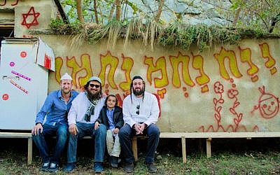 A tale of three friends in Uman. From left to right: Eliav Flataur, Emmanuel Bouzaglou with son Moshe Nachman, and Meir Knafo in the small Ukrainian town in front of typical Breslover graffiti. (Yaniv Salama-Scheer/The Times of Israel)