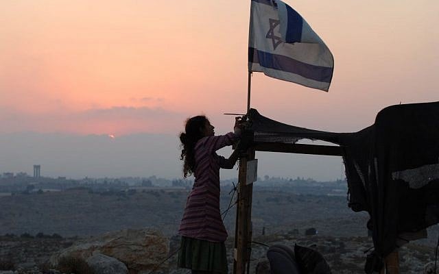 An Israeli girl raises an Israeli flag over a makeshift structure in the illegal outpost of Givat Tzuria near the settlement of Avnei Hefetz, located east of the West Bank Palestinian city of Tulkarem, in this 2009 photograph. (photo credit: Gili Yaari / FLASH90)