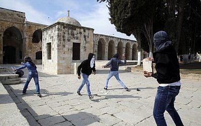 Masked Palestinian youths throw a stones towards Israeli riot police during clashes on February 7, 2014. (Photo credit: Sliman Khader/Flash 90)