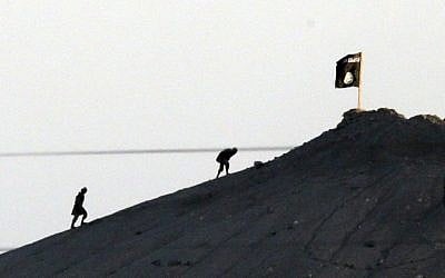This photo, shot with an extreme telephoto lens and through haze from the outskirts of Suruc at the Turkey-Syria border, shows Islamic State members after placing their group's flag on a hilltop at the eastern side of the town of Kobani, Syria, on October 6, 2014. (photo credit: AP Photo/Lefteris Pitarakis)