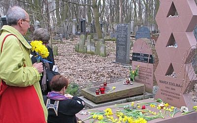Observers placing daffodils at the grave of Marek Edelman, a commander of the Warsaw Ghetto uprising, in Warsaw's Jewish cemetery. (Ruth Ellen Gruber/JTA)