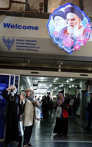 Tourists stand under a picture of Iran's supreme leader, Ayatollah Ali Khamenei (L) and Iran's founder of Islamic Republic, Ayatollah Ruhollah Khomeini (R) on a platform at a station in Tehran after arriving in the Iranian capital on a luxury train from Budapest on October 27, 2014. (photo credit: AFP/ATTA KENARE)