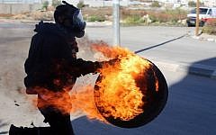 A Palestinian carries a lit tire during clashes between students from Birzeit University and Israeli soldiers in the West Bank on November 6, 2014. photo credit: AFP/ABBAS MOMANI)