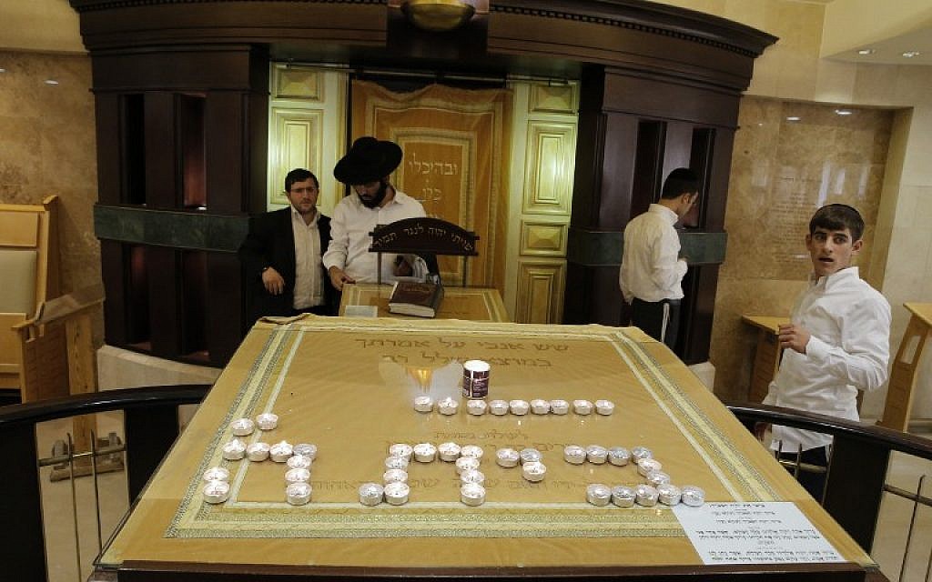 Ultra-orthodox Jewish men stand inside the entrance of a synagogue that was attacked by two Palestinians earlier in the morning in the ultra-Orthodox Har Nof neighborhood in Jerusalem on November 18, 2014. The Hebrew writing in candles says "House of God." (photo credit: AFP/JACK GUEZ)