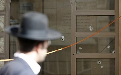 A  Jewish man walks past a synagogue, with bullet holes in its window, that was attacked by two Palestinians earlier in the morning in the Har Nof neighborhood in Jerusalem on November 18, 2014. (photo credit: AFP/ JACK GUEZ)
