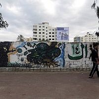 A Palestinian man walks past graffiti showing a masked militant and a destroyed Israeli tank, on November 21, 2014, in Gaza City. (photo credit: AFP/MOHAMMED ABED)