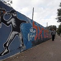 A Palestinian man walks past graffiti showing a masked protester throwing a flower bouquet, in Gaza City, on November 21, 2014. (photo credit: AFP/Mohammed Abed)