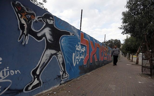 A Palestinian man walks past graffiti showing a masked protester throwing a flower bouquet, in Gaza City, on November 21, 2014. (photo credit: AFP/Mohammed Abed) A Palestinian man walks past graffiti showing a masked protester throwing a flower bouquet, in Gaza City, on November 21, 2014. (photo credit: AFP/Mohammed Abed)