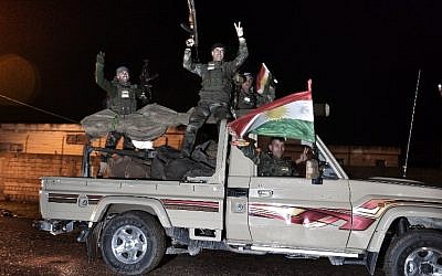 Kurdish peshmerga fighters gesture and wave a Kurdish flag from a military vehicle armed with a heavy infantry weapon as they ride towards the Syrian town of Kobani, also known as Ain al-Arab, from the border town of Suruc, in the Turkish southeastern Sanliurfa province, on October 31, 2014. (photo credit: AFP/STRINGER)