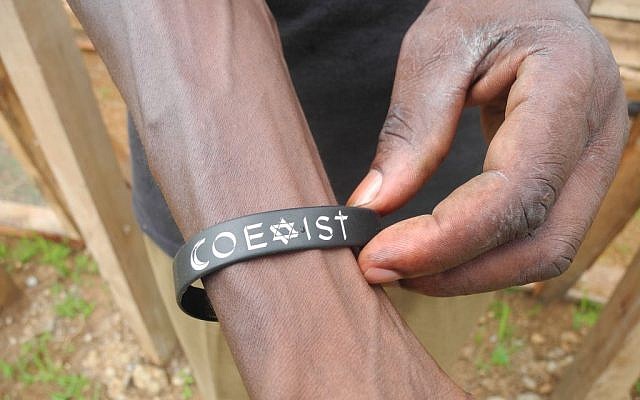 JJ Keki shows off a bracelet that reminds him of the purpose of the Delicious Peace Coffee Cooperative.  (Melanie Lidman/Times of Israel)