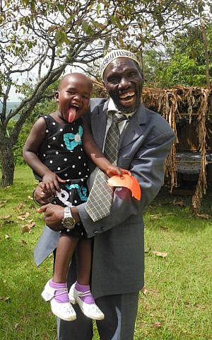JJ Keki, with granddaughter Ranita, serves as a Luganda translator, and reads the Haftorah in Luganda every week. (Melanie Lidman/Times of Israel)