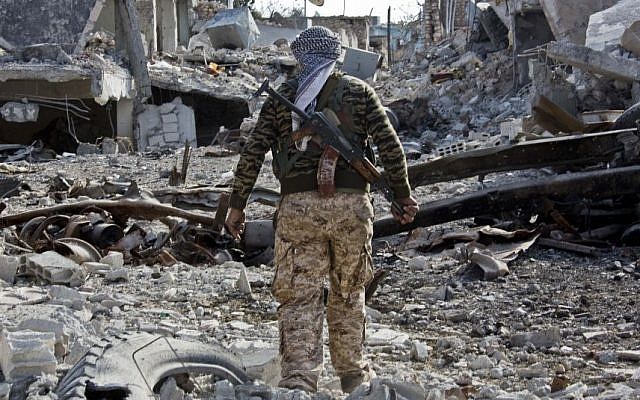 In this Wednesday, Nov. 19, 2014 photo, a Kurdish People's Protection Units (YPG) fighter shows the extent of the damage from a truck bomb in Kobani, Syria. (Photo credit: AP/Jake Simkin)