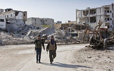 Kurdish People's Protection Units (YPG) soldiers walk near the town entrance circle heading to their strongholds in Kobani, Syria, earlier this year. (photo credit: AP/Jake Simkin)
