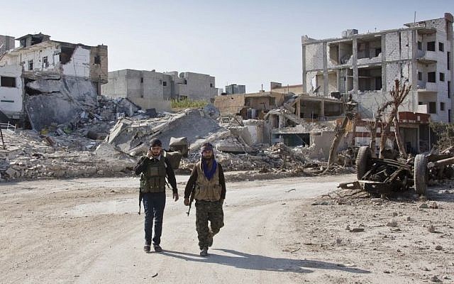 Kurdish People's Protection Units (YPG) soldiers walk near the town entrance circle heading to their strongholds in Kobani, Syria, earlier this year. (photo credit: AP/Jake Simkin)