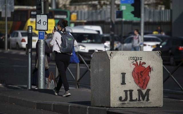 People pass by a graffiti painted concrete block that was placed following the recent hit-and-run terror attacks. (Photo credit: Hadas Parush/Flash90)