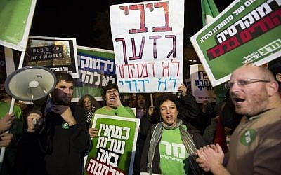 Left-wing activists hold placards and flags as they protest against the "Jewish state" bill near the Prime Minister residence in Jerusalem on November 29, 2014. Some of the placards call Benjamin Netanyahu a racist, and assert that he seeks democracy for Jews only. (Photo credit: Yonatan Sindel/Flash90)