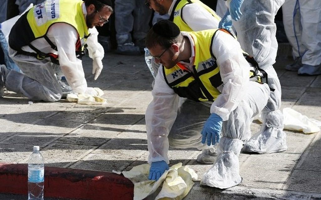 Israeli emergency services personnel gathers blood and other human remains from the sidewalk for proper burial  at the scene of an attack, by two Palestinians, on Israeli worshippers at a synagogue in the ultra-Orthodox Har Nof neighborhood in Jerusalem on November 18, 2014 (photo credit: AFP/Jack Guez)