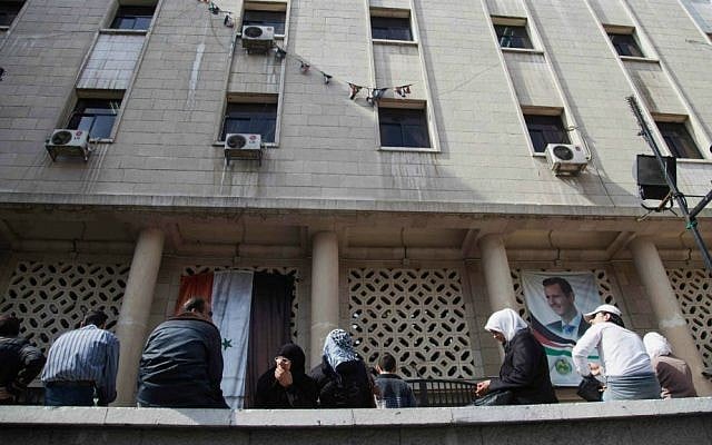 In this Sunday, October 26, 2014 photo, people wait outside a post office building adorned with a picture of President Bashar Assad, in the Syrian capital, Damascus. (photo credit: AP Photo/Diaa Hadid)