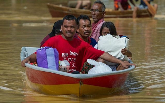 A family ride on a boat through floodwater in Pengkalan Chepa, near Kota Bharu on December 26, 2014 Malaysia's worst flooding in decades forced more than 100,000 people to flee as premier Najib Razak came under fire after photos showed him golfing with US President Barack Obama during the storms. (photo credit: AFP PHOTO) A family ride on a boat through floodwater in Pengkalan Chepa, near Kota Bharu on December 26, 2014. (photo credit: AFP PHOTO)