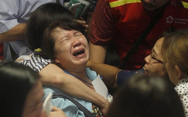 Relatives of passengers of the missing AirAsia flight QZ 8501 react to the news on television about the findings of bodies on the waters near the site where the jetliner disappeared, at the crisis center at Juanda International Airport in Surabaya, East Java, Indonesia, Tuesday December 30, 2014. (photo credit: AP/Trisnadi)