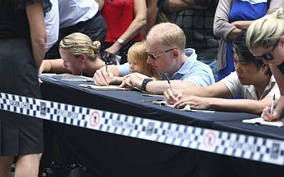 People sign tributes at a makeshift memorial after shootings during a siege at the Lindt Cafe at Martin Place in the central business district of Sydney Australia. Tuesday, Dec. 16, 2014. Tearful Australians laid mounds of flowers at the site where a gunman held hostages for 16 hours at a popular Sydney cafe. The siege ended early Tuesday with a barrage of gunfire that left two hostages and the Iranian-born gunman dead, and a nation that has long prided itself on its peace rocked to its core. (photo credit: AP Photo/Steve Christo)