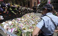 A police officer looks at flower tributes placed at a temporary memorial site close to the Lindt Cafe in the central business district of Sydney, Australia, Wednesday, Dec. 17, 2014. (photo credit: AP/Rob Griffith)