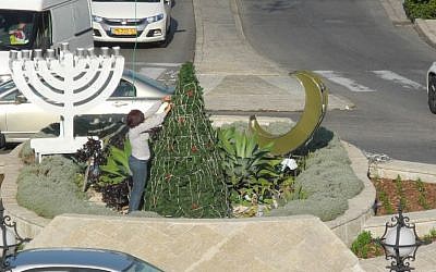 A worker puts the finishing touches on a display of a Christmas tree, a crescent, and a menorah at the main traffic circle in front of the Bahai Gardens in Haifa for the Festival of Festivals, December 2014. (photo credit: Melanie Lidman/Times of Israel)