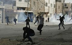 Palestinian rioters throw stones during clashes with Israeli soldiers in the West bank town of Hebron, on November 21, 2014. (Photo credit: Ibrahim Hmouz/Flash90)
