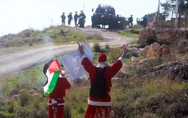 Palestinian protesters wearing Santa Claus costumes wave during a protest against Israel's security barrier outside the West Bank village of Bil'in, near Ramallah, Friday, December 26, 2014 (Photo credit: STR/Flash90)