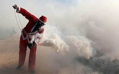 A Palestinian protester wearing a Santa Claus costume holds a tear gas canister during a protest against Israel's security barrier outside the West Bank village of Bil'in, near Ramallah, Friday, December 26, 2014 (photo credit: STR/Flash90)