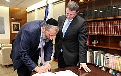 Shas party leader Aryeh Deri signs a letter resigning from the Knesset, as Speaker Yuli Edelstein looks on, December 30, 2014. (Photo credit: Isaac Harari/Knesset Spokesperson)