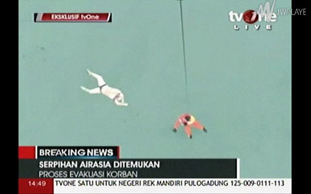 In this image taken from video released by TV One, a rescuer is lowered on rope from a hovering helicopter near a body in Java Sea waters, Indonesia Tuesday, December 30, 2014. (photo credit: AP/TV One via AP Video)
