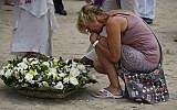 A relative of a victim from the Asian tsunami holds back her tears as she lays a white rose on the beach during a commemoration and religious ceremony for German, Austrian and Swiss victims of the Asian tsunami, in Khao Lak, Thailand, Friday, Dec. 26, 2014. (Photo credit: AP/Wong Maye-E)