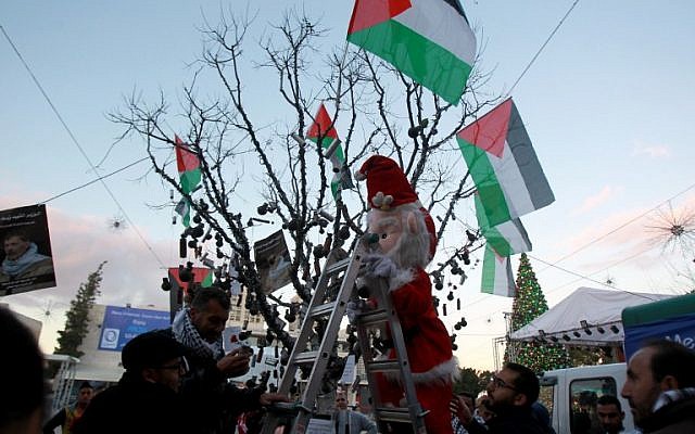 A Palestinian dressed up as Father Christmas decorates a "popular resistance" Christmas tree with tear gas canisters and Palestinian flags at Manger Square, outside the Church of the Nativity, traditionally believed by Christians to be the birthplace of Jesus Christ, in the West Bank biblical city of Bethlehem, on December 23, 2014. (photo credit: AFP PHOTO / MUSA AL-SHAER) A Palestinian dressed up as Father Christmas decorates a "popular resistance" Christmas tree with tear gas canisters and Palestinian flags at Manger Square, outside the Church of the Nativity, traditionally believed by Christians to be the birthplace of Jesus Christ, in the West Bank biblical city of Bethlehem, on December 23, 2014. (photo credit: AFP PHOTO / MUSA AL-SHAER)