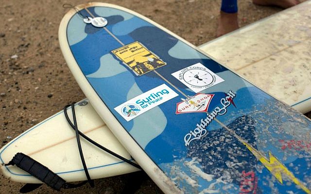 In this Thursday, November 27, 2014 photo, Palestinian Mohammed Abu Jayyab, 41, stands next to surf boards, one with logos of world organizations that donated them to the Palestinians in Gaza, including Surfing for Peace, on the beach of Gaza City. (photo credit: AP Photo/Khalil Hamra)