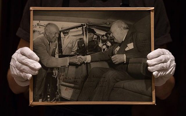 In this photo taken Tuesday, Dec. 9, 2014, a member of Sotheby's staff poses for a picture with a photograph of U.S. President Dwight D. Eisenhower and Churchill with dedication: "for Christopher Soames, with personal regards, Dwight Eisenhower” at the auction house in London, England. (photo credit: AP Photo/Tim Ireland) In this photo taken Tuesday, Dec. 9, 2014, a member of Sotheby's staff poses for a picture with a photograph of U.S. President Dwight D. Eisenhower and Churchill with dedication: "for Christopher Soames, with personal regards, Dwight Eisenhower” at the auction house in London, England. (photo credit: AP Photo/Tim Ireland)