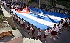 Young students carry a large Cuban flag, as they attend a parade through the streets of Gibara, Cuba. January 20, 2014. (photo credit: Moshe Shai/Flash90)