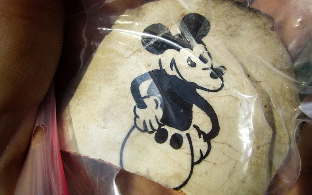 Fragment of a ceramic cup excavated at the former Nazi death camp Sobibor, with an image of Mickey Mouse. The artifact was unearthed by archeologists Wojtek Mazurek and Yoram Haimi in 2014 (Matt Lebovic/The Times of Israel). Fragment of a ceramic cup excavated at the former Nazi death camp Sobibor, with an image of Mickey Mouse. The artifact was unearthed by archeologists Wojtek Mazurek and Yoram Haimi in 2014 (Matt Lebovic/The Times of Israel).