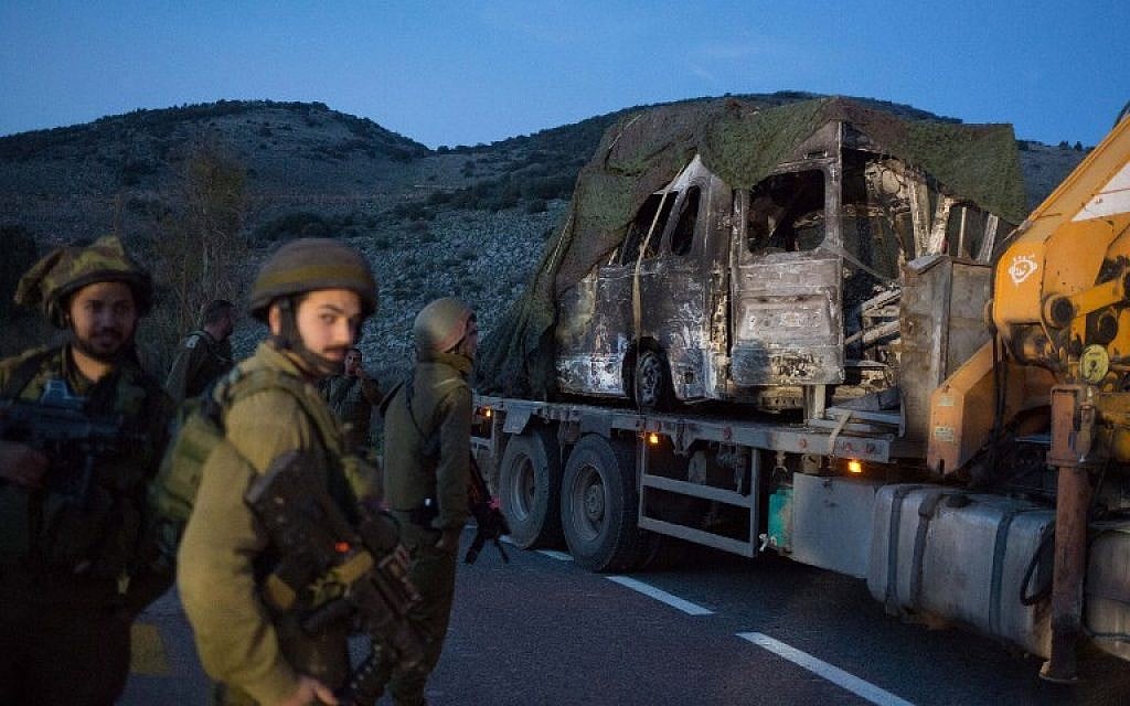 Israeli soldiers look at a burned-out vehicle loaded onto the back of a truck near Ghajar after it was removed from the seen of a Hezbollah missile attack along the Israel-Lebanon border on January 28, 2015. (AFP/MENAHEM KAHANA)