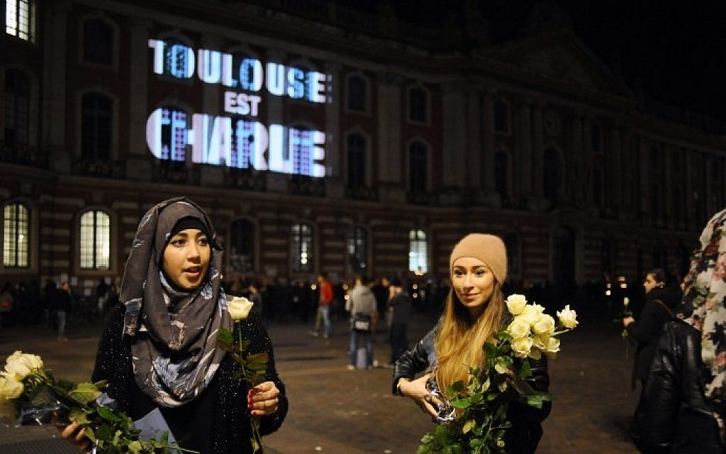 Women give out white roses near the Capitole building in Toulouse, southern France, where on the facade is projected the words "Toulouse est Charlie" (Toulouse is Charlie), on January 9, 2015 (Photo credit: Remy Gabalda/AFP)